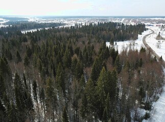 Aerial view of the winter and snowy landscape in Russia. Winter and snowy forest, top view of the horizon, spruce forest, pine trees, road and village. Captured from above with a drone. 