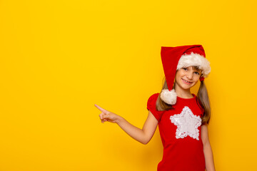 Little girl wearing Santa hat pointing towards blank space