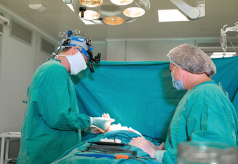 Surgeon and his assistant performing cosmetic surgery on nose in hospital operating room. Nose...