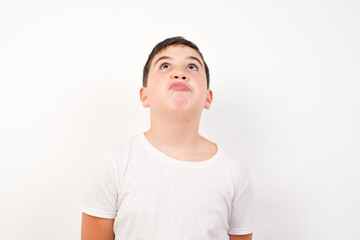 Caucasian young boy standing against white background looking up as he sees something strange.