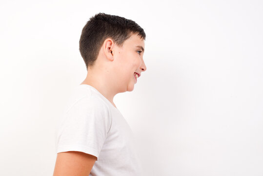 Profile of smiling Caucasian young boy standing against white background  with healthy skin, has contemplative expression, ready to have outdoor walk.