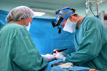 Surgeon and his assistant performing cosmetic surgery on nose in hospital operating room. Nose...