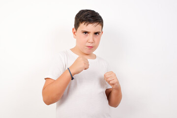 Portrait of attractive Caucasian young boy standing against white background  holding hands in front of him in boxing position going to fight.