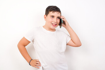 Portrait of successful joyful Caucasian young boy standing against white background talking on mobile phone with friend. Lifestyle and communication concept