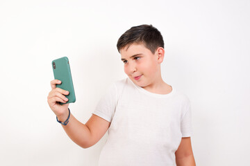 Isolated shot of pleased cheerful Caucasian young boy standing against white background, makes selfie with mobile phone. People, technology and leisure concept