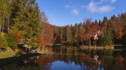 Lake in the autumn mountains among yellow and red trees with a wooden house by the water