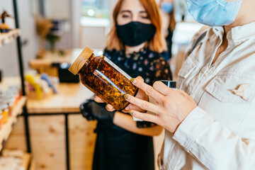 A female shop assistant serving blond curly customer in a zero-waste shop. Safety in public place while covid-19 epidemic. Close up. Selective focus.