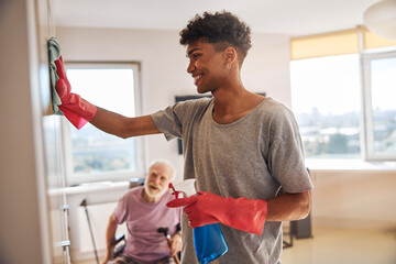 Smiling volunteer cleaning the room of a senior man