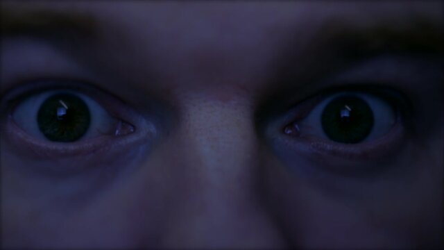 A man wakes from a nightmare. The spooky eyes are closed and in the shadows when something causes the man to awake suddenly shocked with creepy eyes wide open.