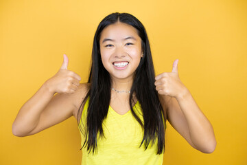 Young beautiful asian woman over yellow isolated background success sign doing positive gesture...