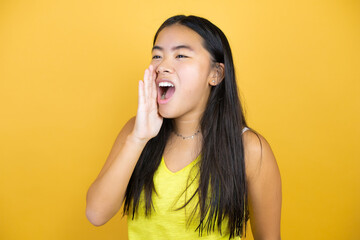 Young beautiful asian woman over yellow isolated background shouting and screaming loud to side with hand on mouth