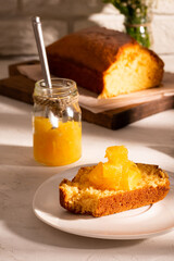 A jar of orange jam and a cake on a white table