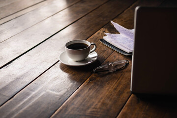 A coffee cup on the desk that has glasses and a notebook computer