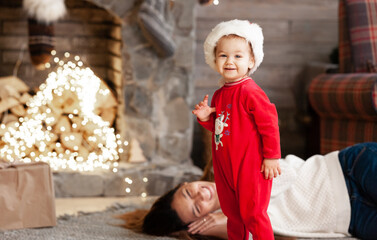 Little girl in santa costume is looking in camera near the christmas lights and mom smiling next to her. New year eve