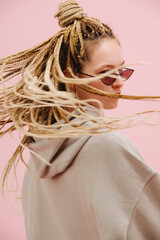 Turning woman in sunglasses waving her stylish blond afro braids over pink
