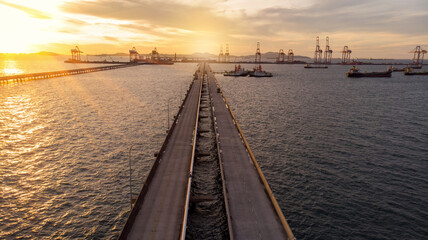 Aerial view of  Bridge for export import cargo to crane at sun set , Bride road to international cargo dock sea port.