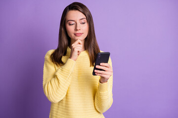 Photo portrait of woman thinking holding phone in one hand looking touching face chin with finger isolated on vivid purple colored background