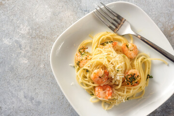 Spaghetti with shrimps, parsley and garlic, Mediterranean seafood appetizer on a plate, rustic gray background with copy space, high angle view from above
