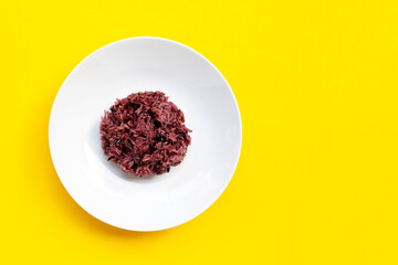 Black sticky rice on white ceramic dish on yellow background.