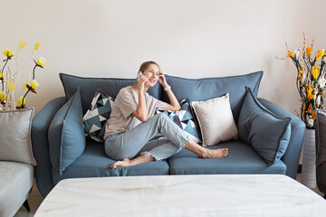 Young beautiful woman stylish wearing on gray textile sofa at home. Attractive slim female in domestic situation, staying home, resting on couch in her apartment. Background, copy space, close up.