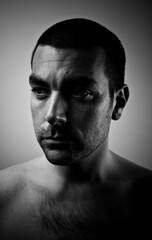 Short haired dark man with serious look. Black and white studio portrait in dark setting. Grey background. 