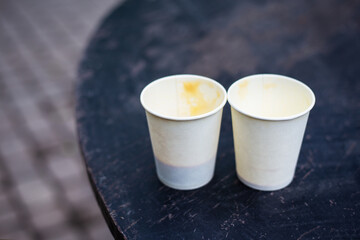 Two plastic glasses with coffee stand on the street on a wooden table. Close-up.
