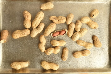 Unpeeled organic peanuts, close-up, on a metal tray.