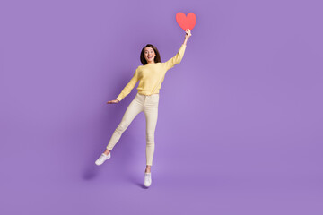 Photo portrait full body view of excited girl holding big red heart card jumping up isolated on vivid violet colored background © deagreez