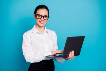 Portrait of attractive cheerful geek specialist girl holding in hands laptop browsing isolated over bright blue color background