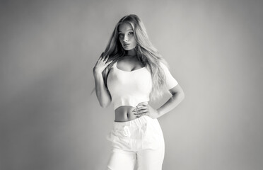 Black-white photo of a pretty blonde in white sportswear posing in the studio