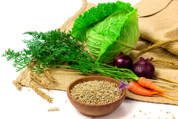 Rye seeds in wooden bowl, dry ears of rye, fresh carrot, savoy cabbage and green onion on sackcloth on white background. Organic, healthy food concept