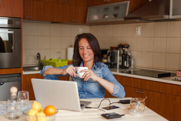 Happy woman using laptop during coffee time in the kitchen.