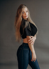 Luxury blonde dressed in a short top and jeans posing in the studio on a gray background