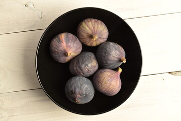 Ripe dark blue organic figs on a ceramic plate, close-up, on a wooden table.