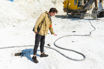 the traveler stands in front of a large excavator. a man stands next to a high-voltage wire in the middle of a white sand industrial quarry.