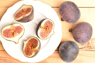 Ripe dark blue organic figs on a ceramic plate, close-up, on a wooden table.