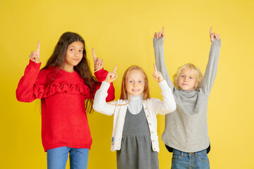 Obraz premium Pointing, choosing. Portrait of little caucasian children isolated on yellow studio background with copyspace. Beautiful teen models. Concept of human emotions, facial expression, sales, ad, youth.