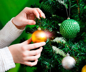 Girl's hands hang a golden sliding ball on a tree spruce branch