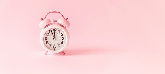 On a retro alarm clock at five minutes to midnight. Five minutes before the start of a new day, new month or new year. Final countdown. Pink copy space background. 