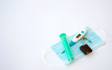Thermometer, padlock and a syringe lying on a surgical face mask