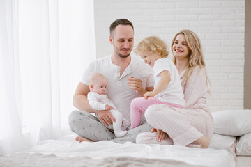 A young Caucasian family with two children daughters in a white home interior. Home clothes.