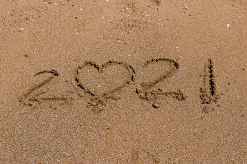 number 2021 is written on the sand at sea.. 2021