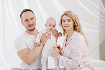 Obraz na płótnie Canvas A young Caucasian family with a newborn baby daughter in the bedroom. White light home interior.