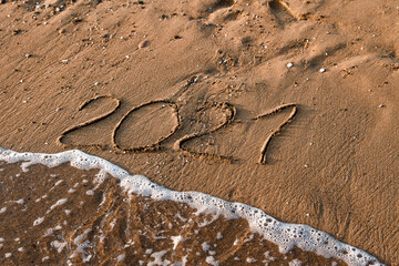 number 2021 is written on the sand at sea. waves and sand. 2021