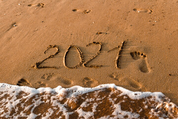 number 2021 is written on the sand at sea. waves and sand. 2021