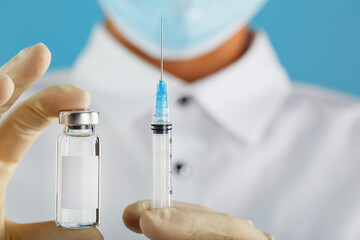 A doctor in rubber gloves holds an ampoule with a vaccine and a syringe, close-up.