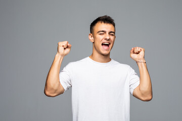 Fototapeta premium Great news. Happy young man gesturing and smiling while talking on the mobile phone and standing against grey background