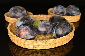 Ripe dark blue organic plums, close-up, on a black background.