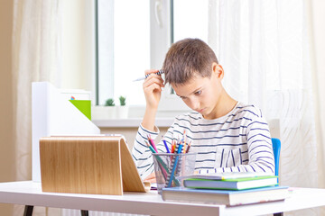 Kid with digital tablet computer writing, doing homework at white desk. Online learning, remote education, distance lessons at home - obrazy, fototapety, plakaty