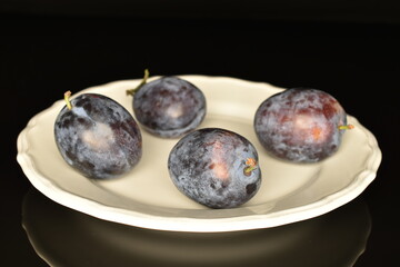 Ripe dark blue organic plums, close-up, on a black background.